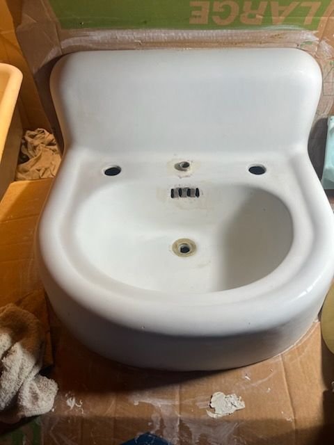 White ceramic sink with faucet holes, sitting in a cardboard box.