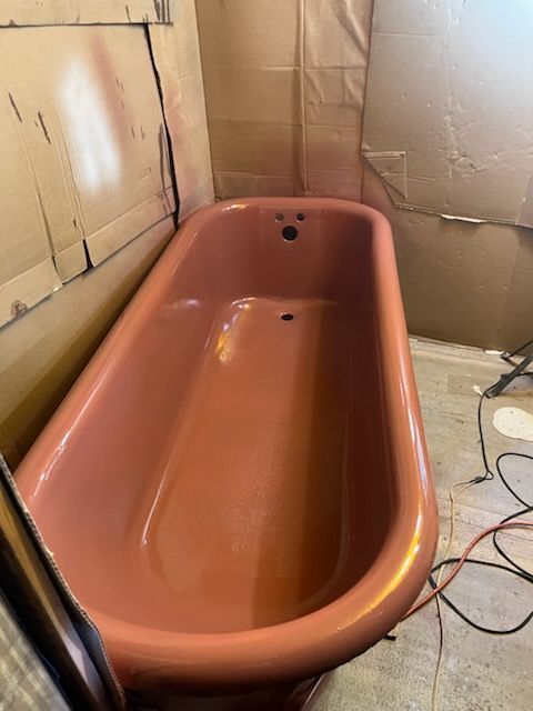 Rust-colored bathtub against unfinished walls on a construction site, with cords on the floor.