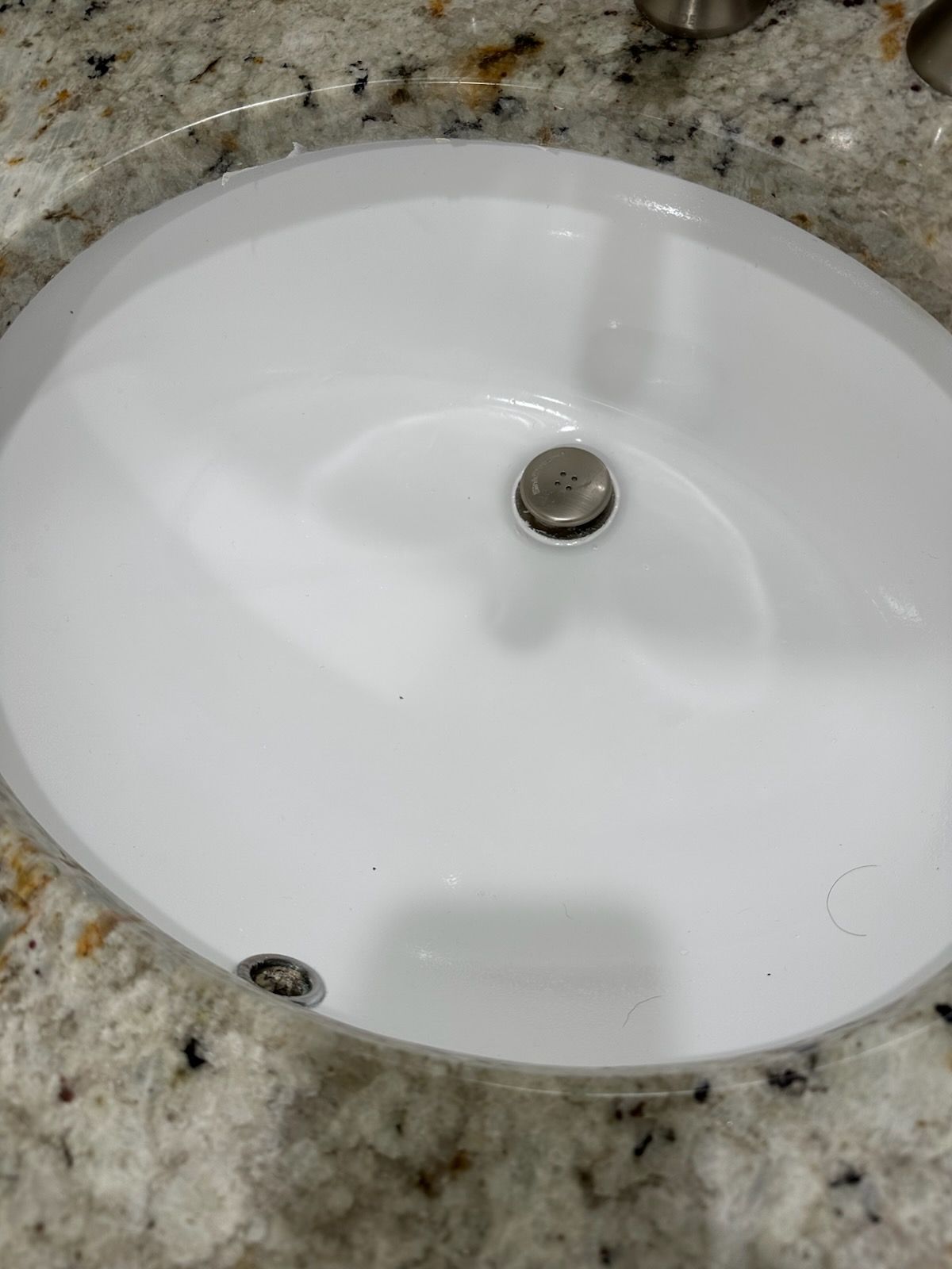White oval bathroom sink set in a speckled granite countertop, with drain stopper visible.