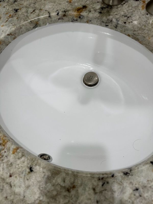 White oval bathroom sink set in a speckled granite countertop, with drain stopper visible.