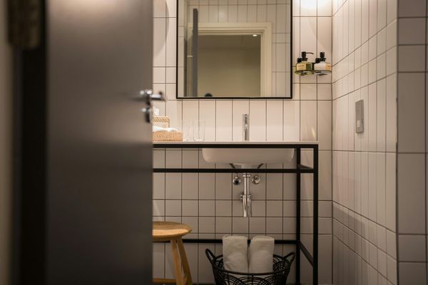 Small tiled bathroom with a mirror, sink, towel rack, stool, and basket in soft neutral tones