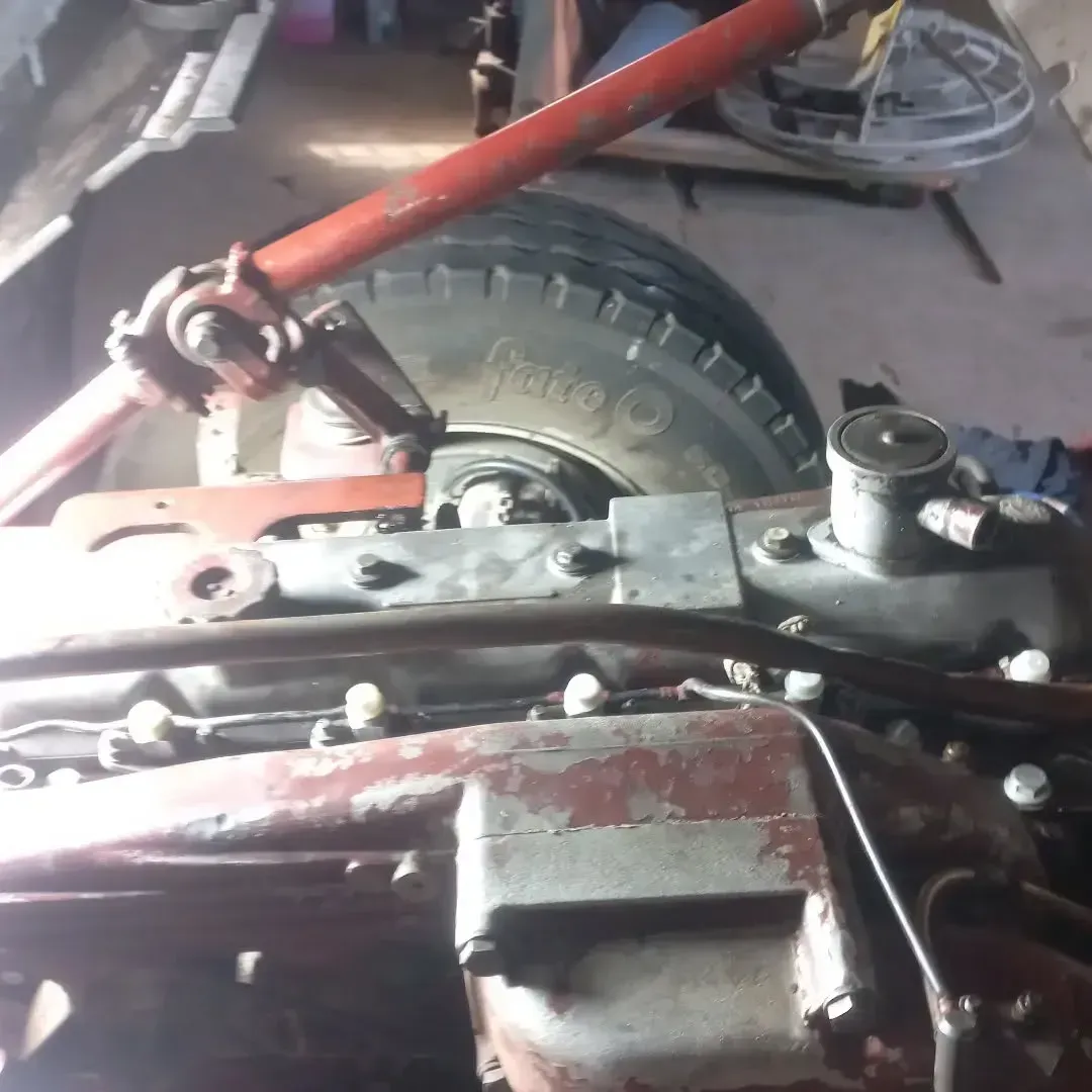 Primer plano del motor de un tractor rojo con piezas mecánicas y un neumático al fondo.