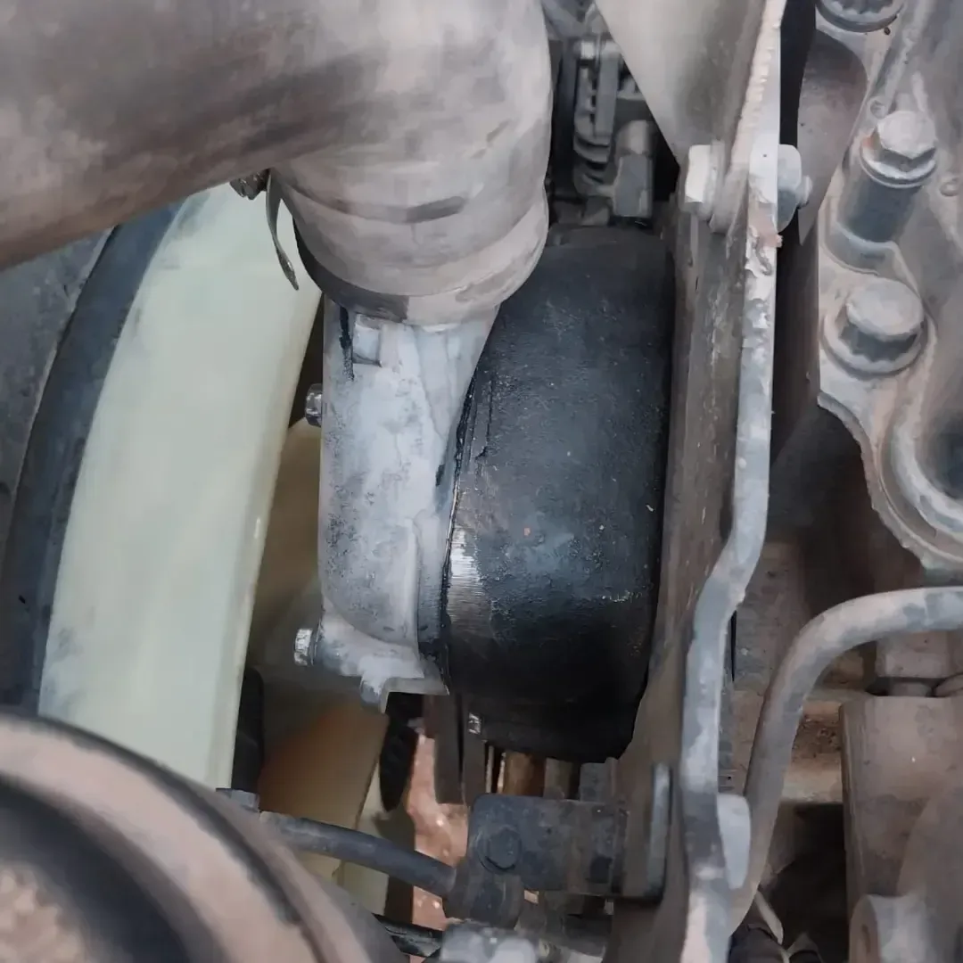 Primer plano de un componente del motor de un camión con residuos blancos y acumulación de hollín alrededor de una conexión de manguera de goma.