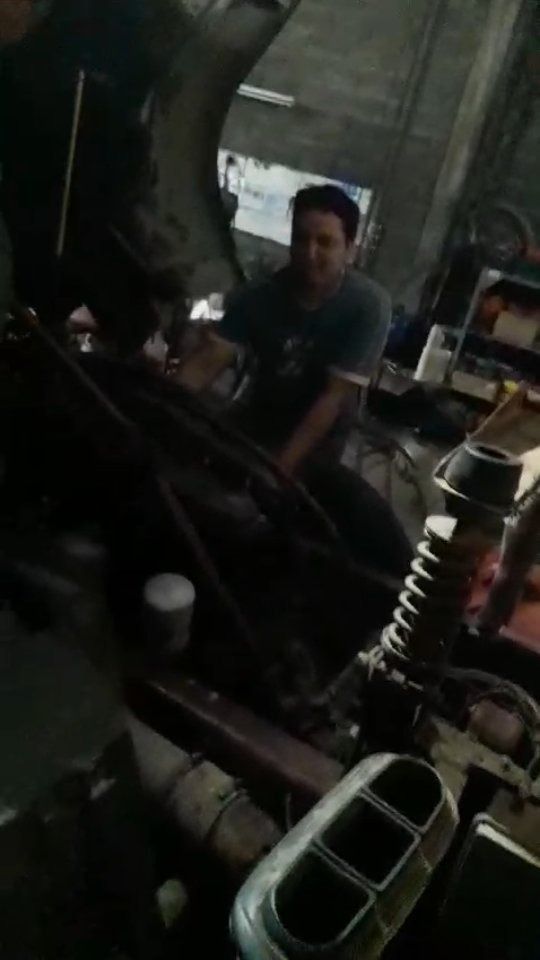 Una persona trabaja en el motor de un vehículo dentro de un garaje con poca luz.