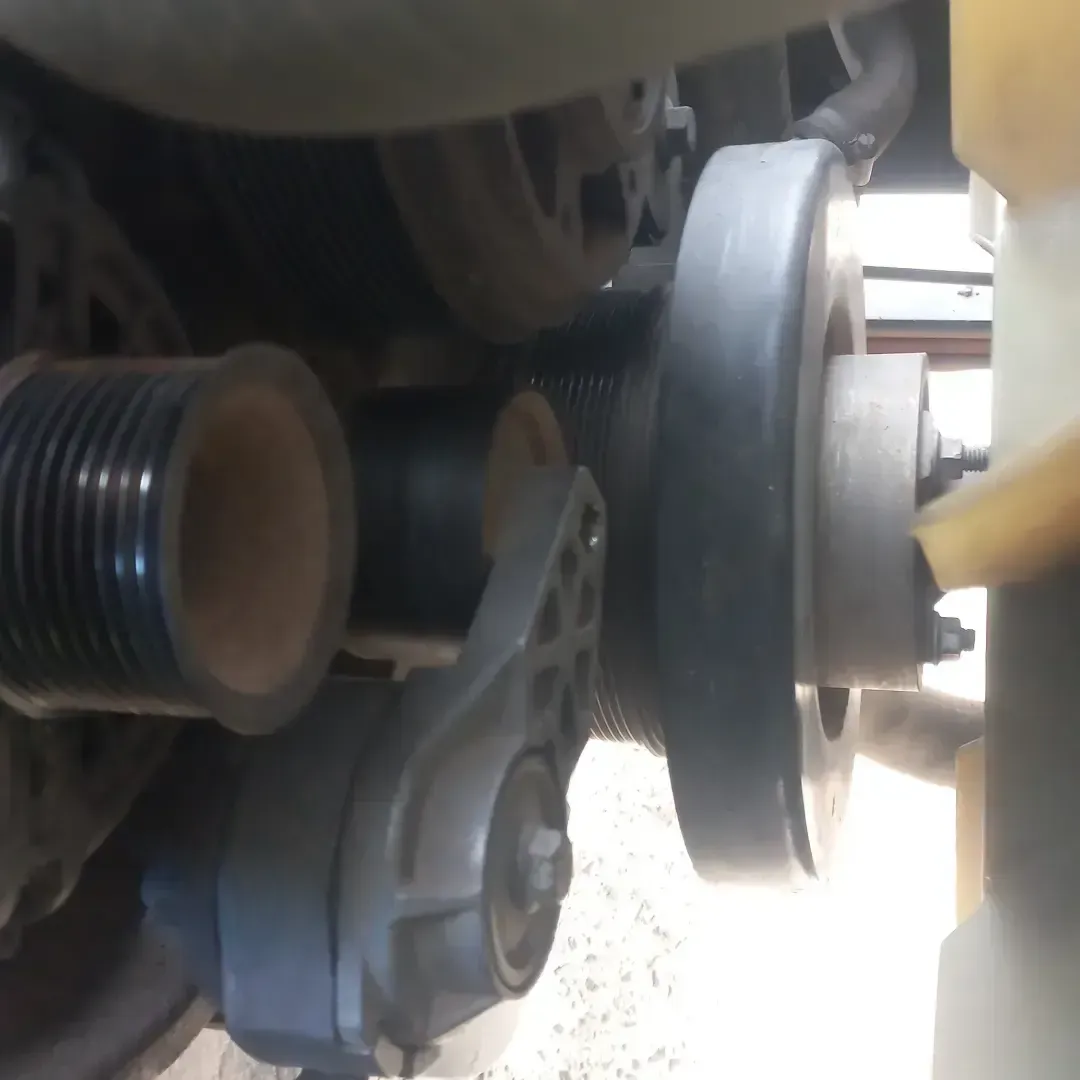 Vista en primer plano del sistema de correa serpentina del motor de un vehículo, que incluye poleas y un tensor de correa.