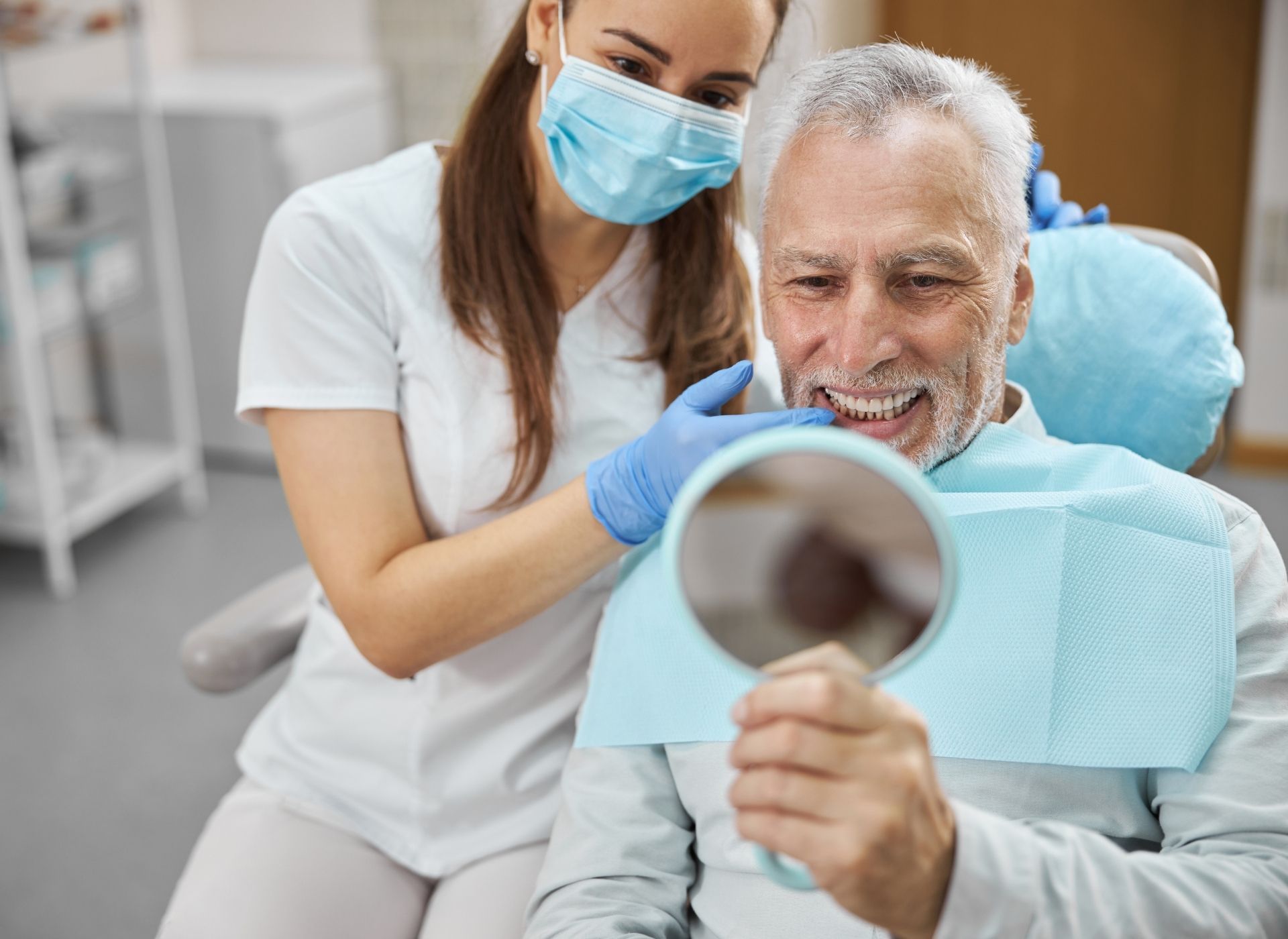 Dentist in mask and gloves showing senior patient his teeth in a mirror.