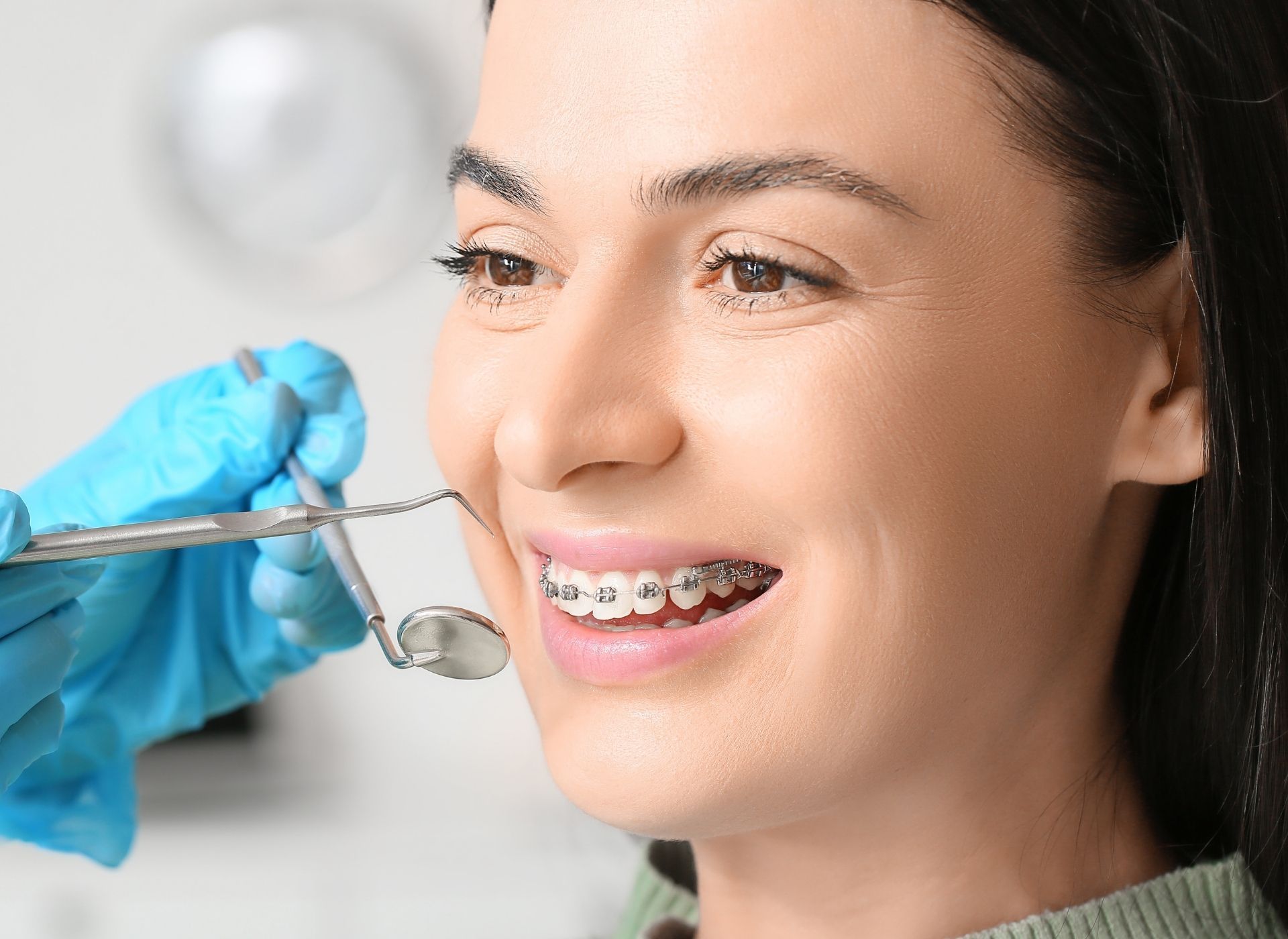 Woman with braces has teeth examined by a dentist in an office setting.
