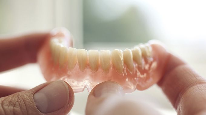 Hands holding a set of upper dentures, the teeth white, the gums pink.