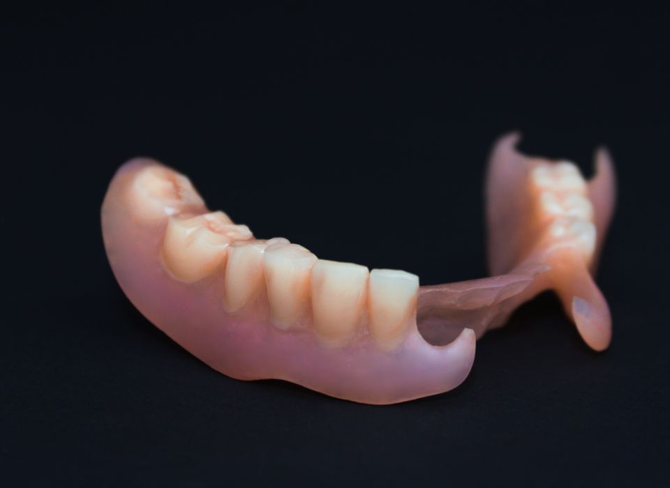 Partial denture on a black surface, pink gum-like material, and white teeth.