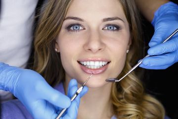 Woman at the dentist, receiving an exam. Dentist's gloved hands hold tools examining her teeth.