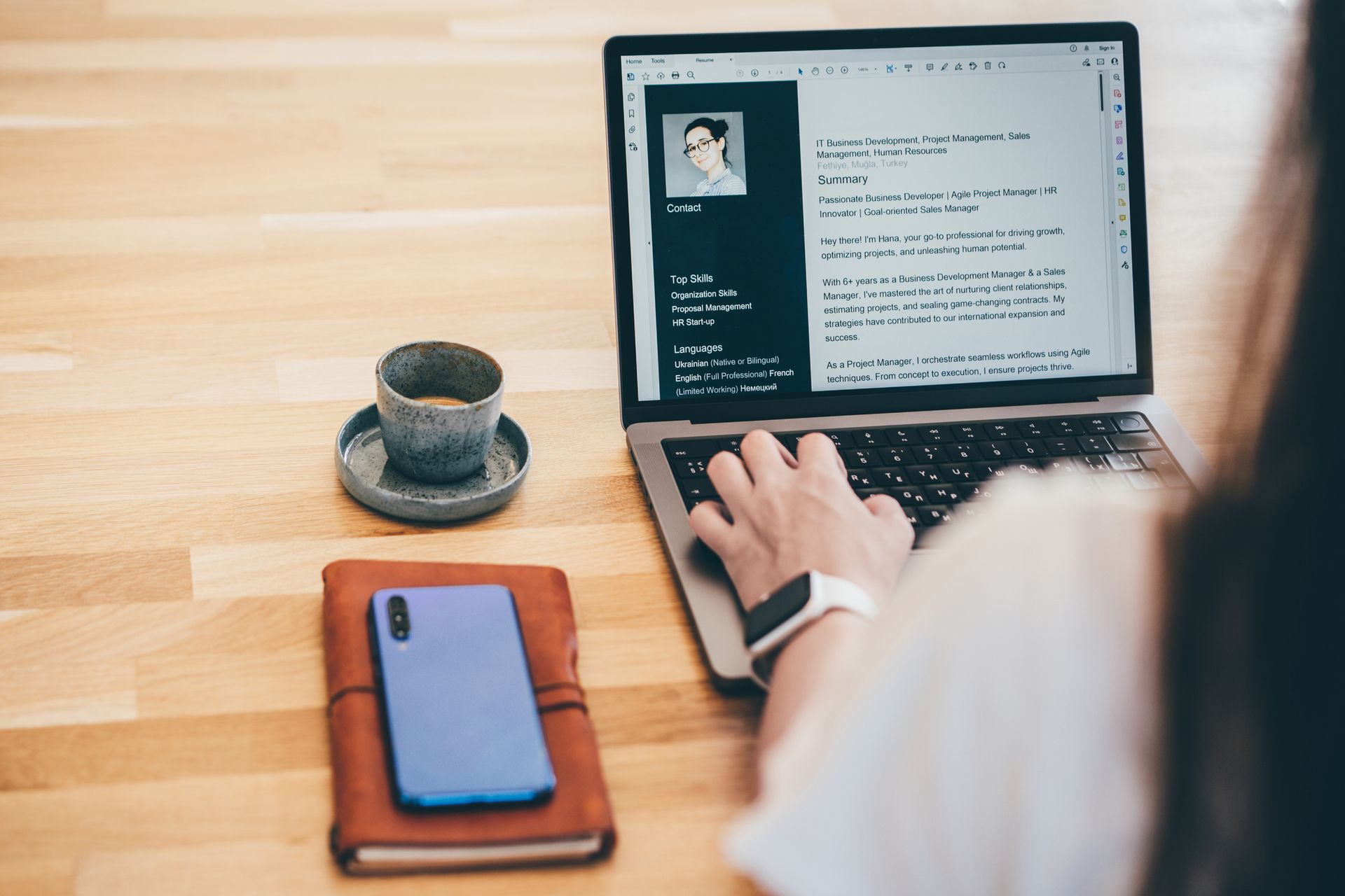 A woman is typing on a laptop next to a cup of coffee and a cell phone.