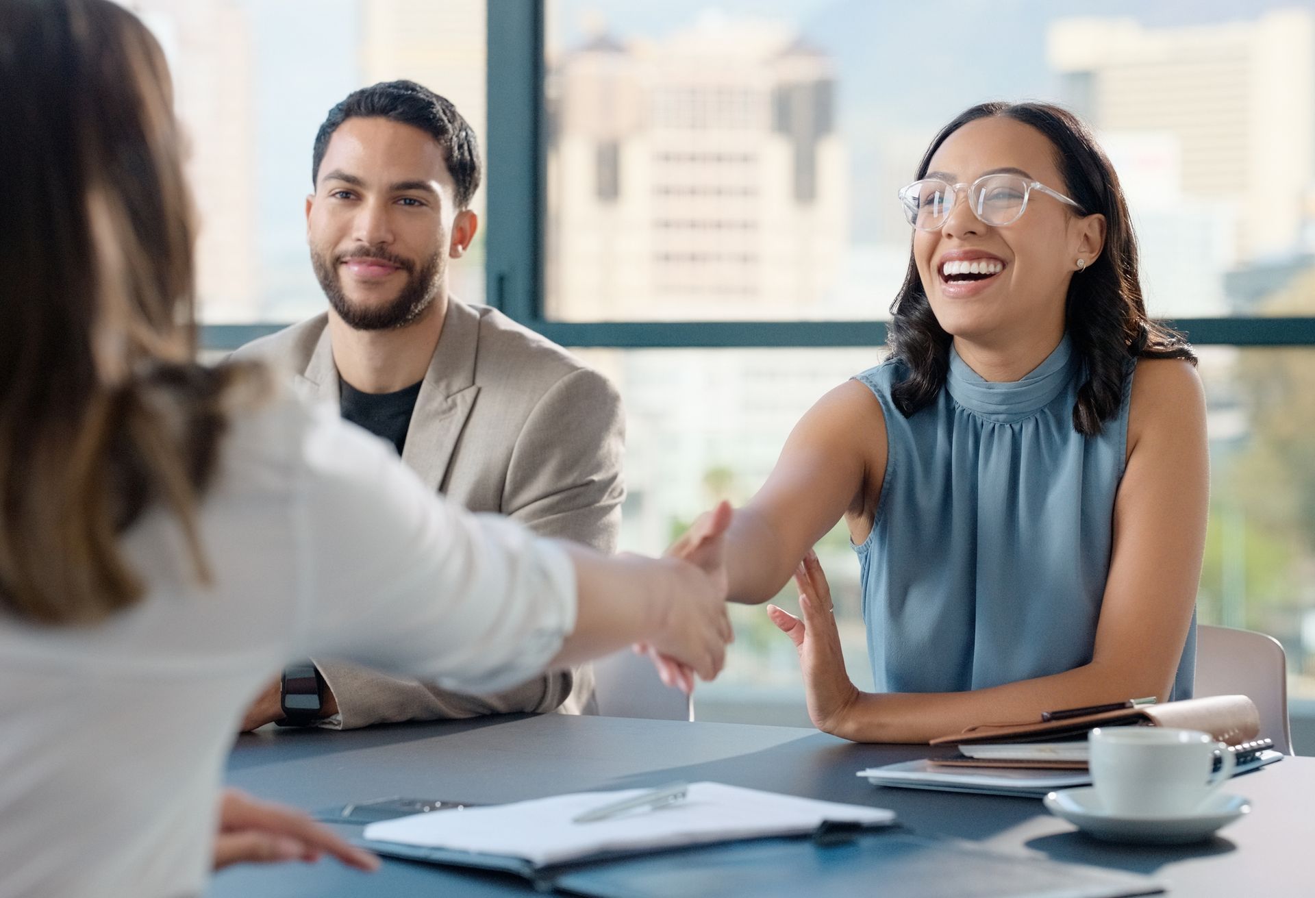 A woman is shaking hands with a man and woman while sitting at a table.