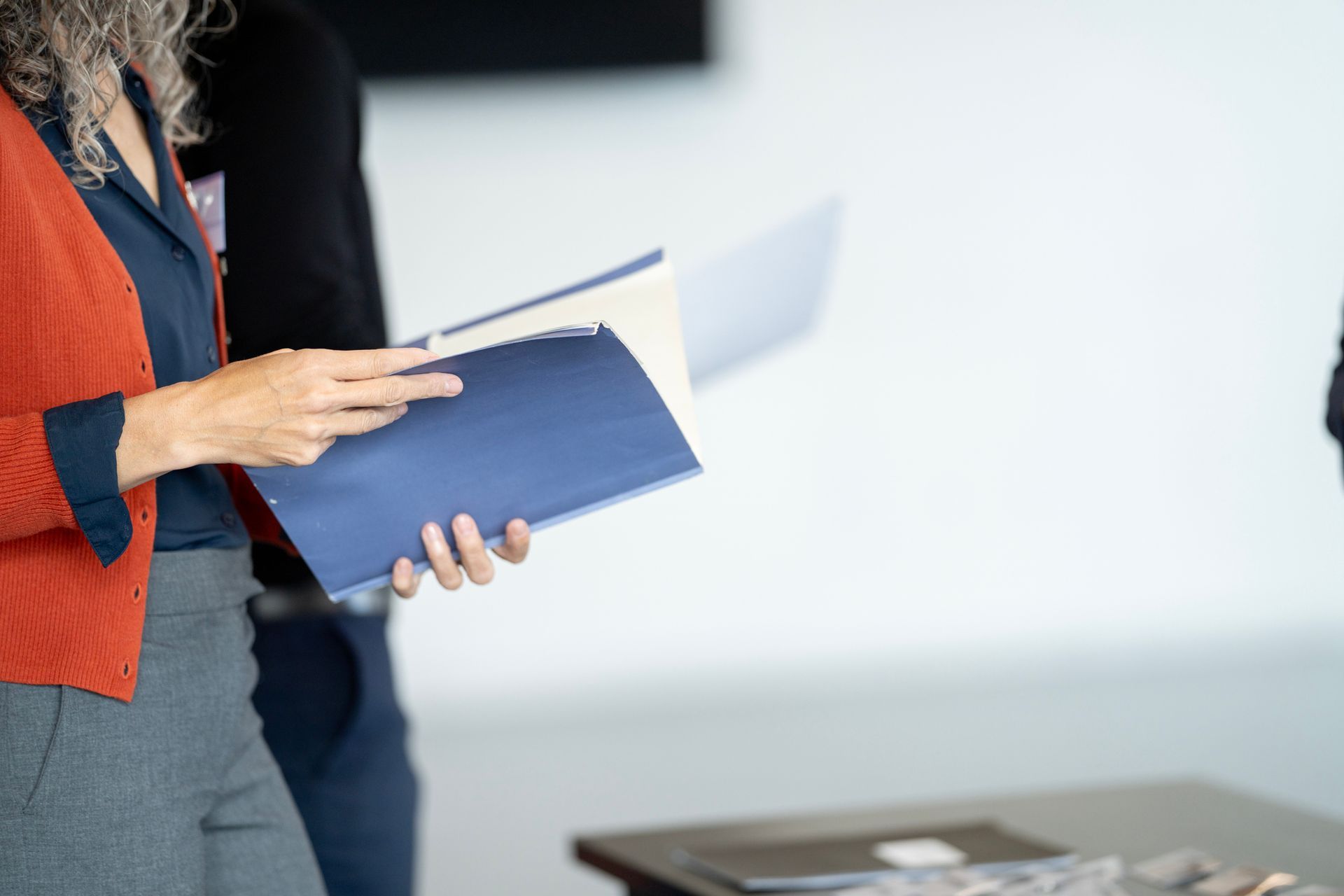 A person in a red cardigan flips through a blue folder.
