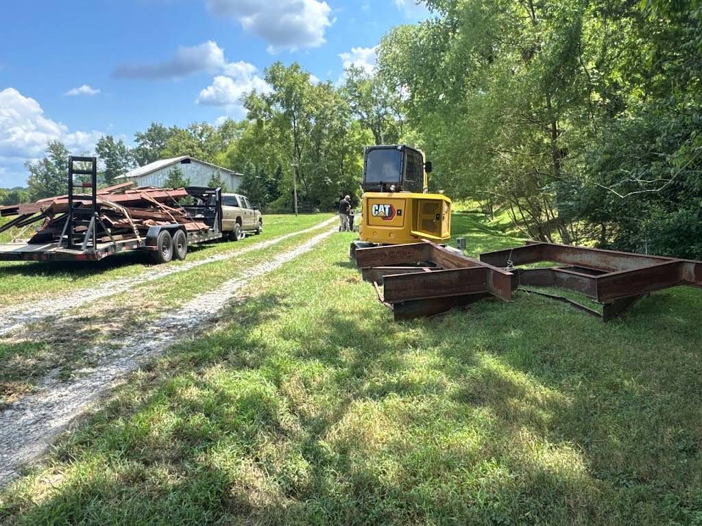 A Cat grinder and trailer with debris are on a grassy area, likely clearing land.