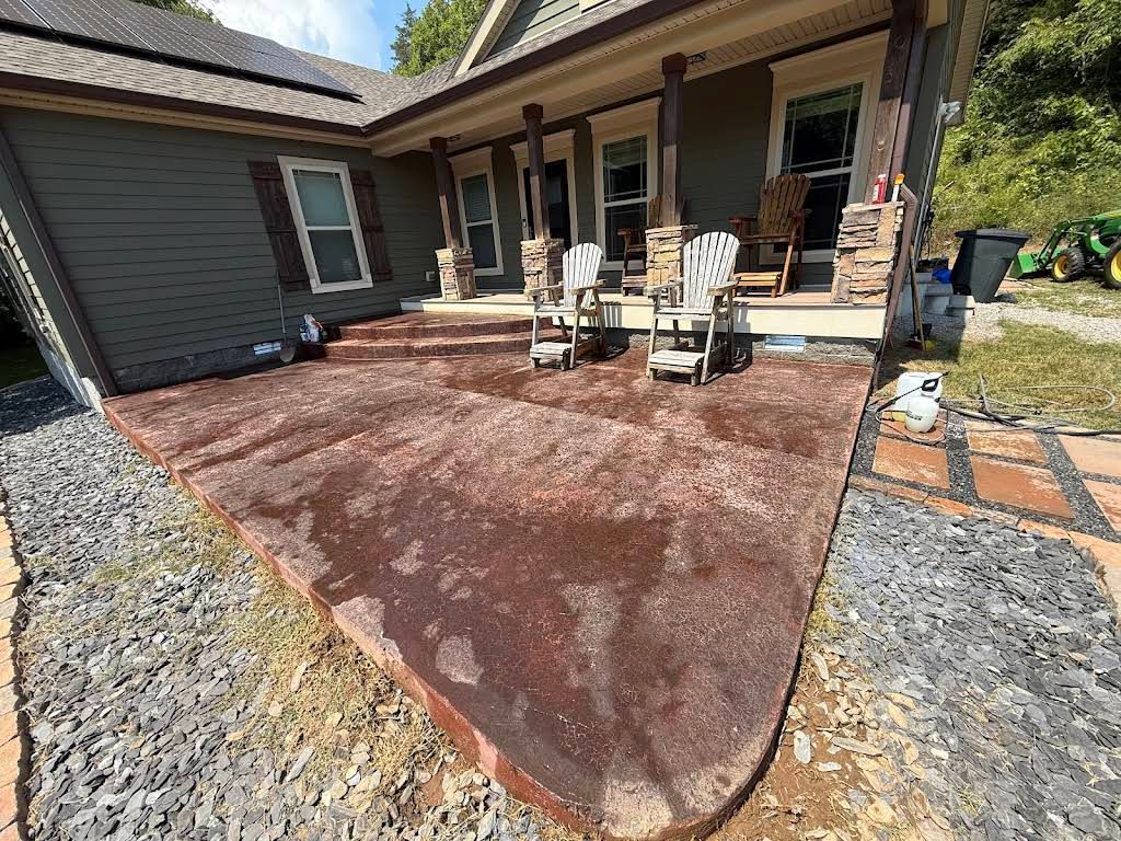 Front porch with two chairs on a red concrete patio. House is gray with stone columns, lawn on the side.