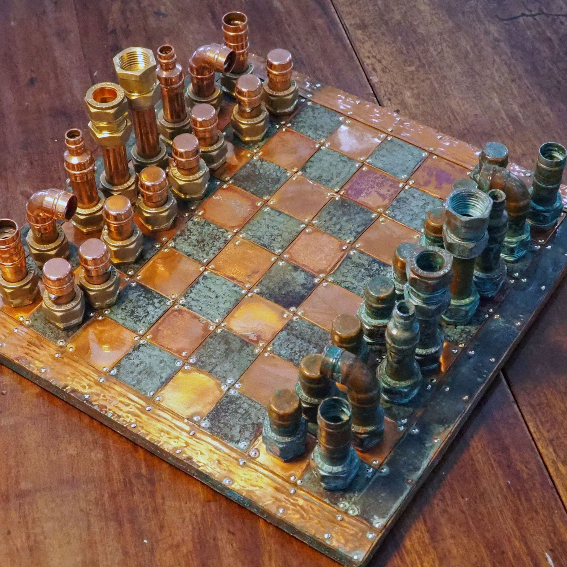 A chess set made from copper. The board is made from shinny and tarnished copper - given the two 'players' their distinct colours. The pieces are made from copper plumbing piping and brass nuts and bolts. 