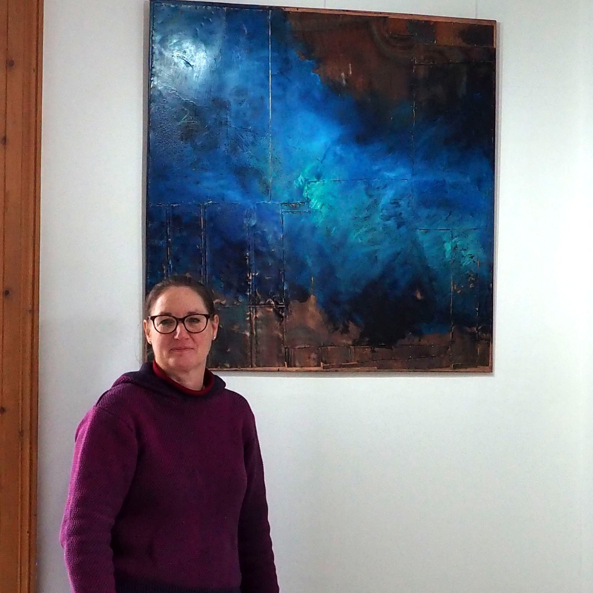 Artist Nicky Huxham standing to the bottom left of one of her large paintings on copper.
