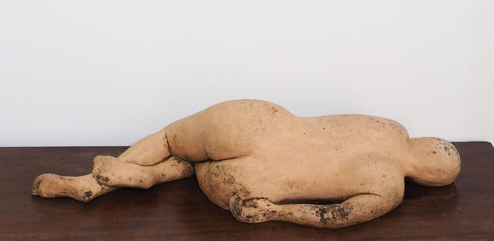 The back of a reclining sculpture of a naked woman. Looks flesh colour and is on a wood surface.