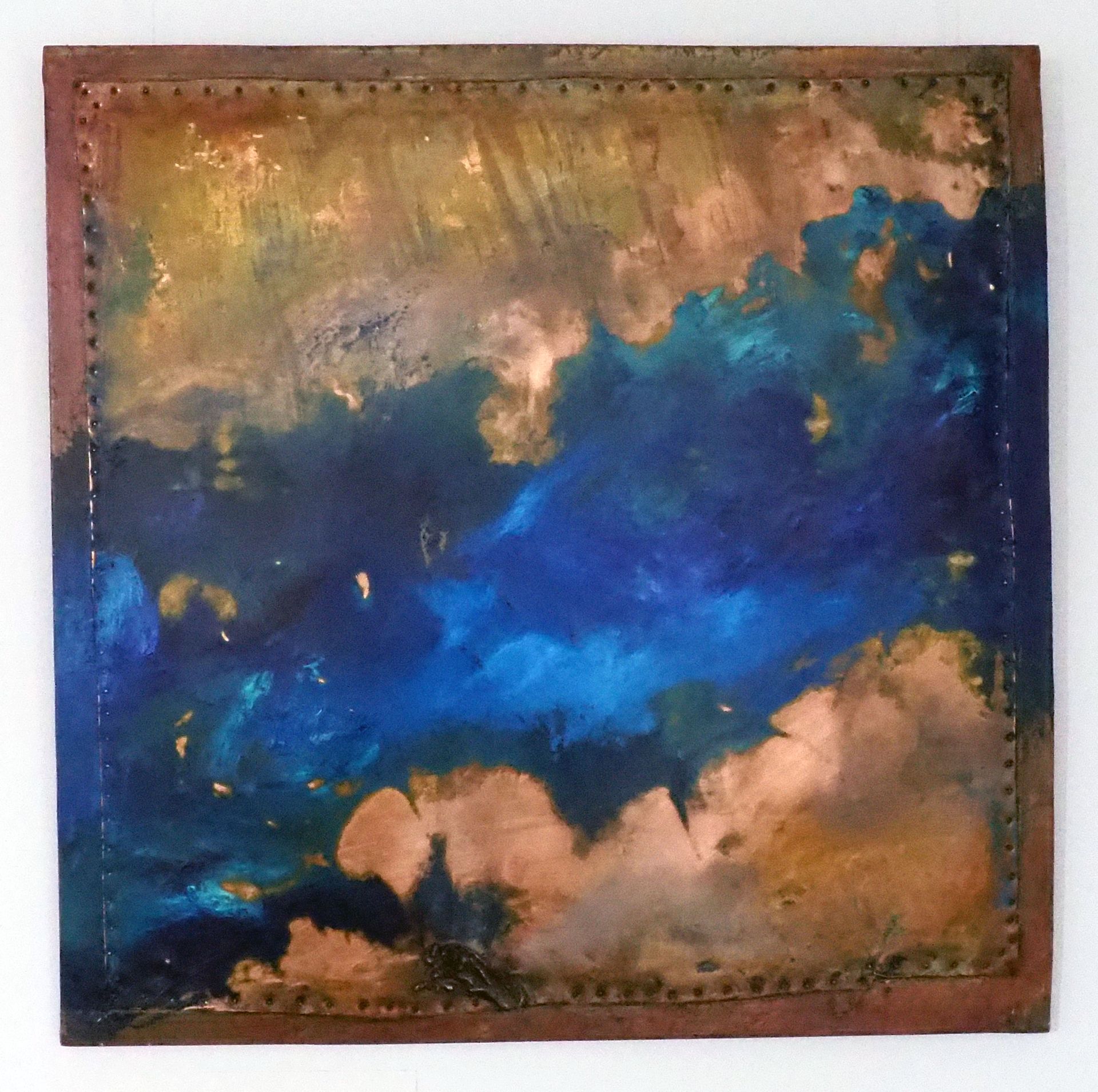 A square copper panel pinned onto a copper coloured board. The copper is tarnished in places. There is blue with a bit of aqua painted roughly diagonally over the piece. 