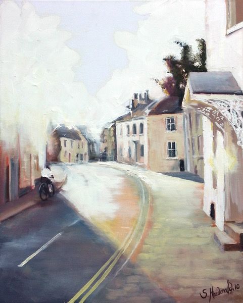 Painting of an old street that is winding off to the left. There are old Georgian houses on both sides. The bottom left corner is in shadow . A cyclist is riding out of the shadow into the light. The light is coming in from the top left. The main colours are white, cream, peach and greys.