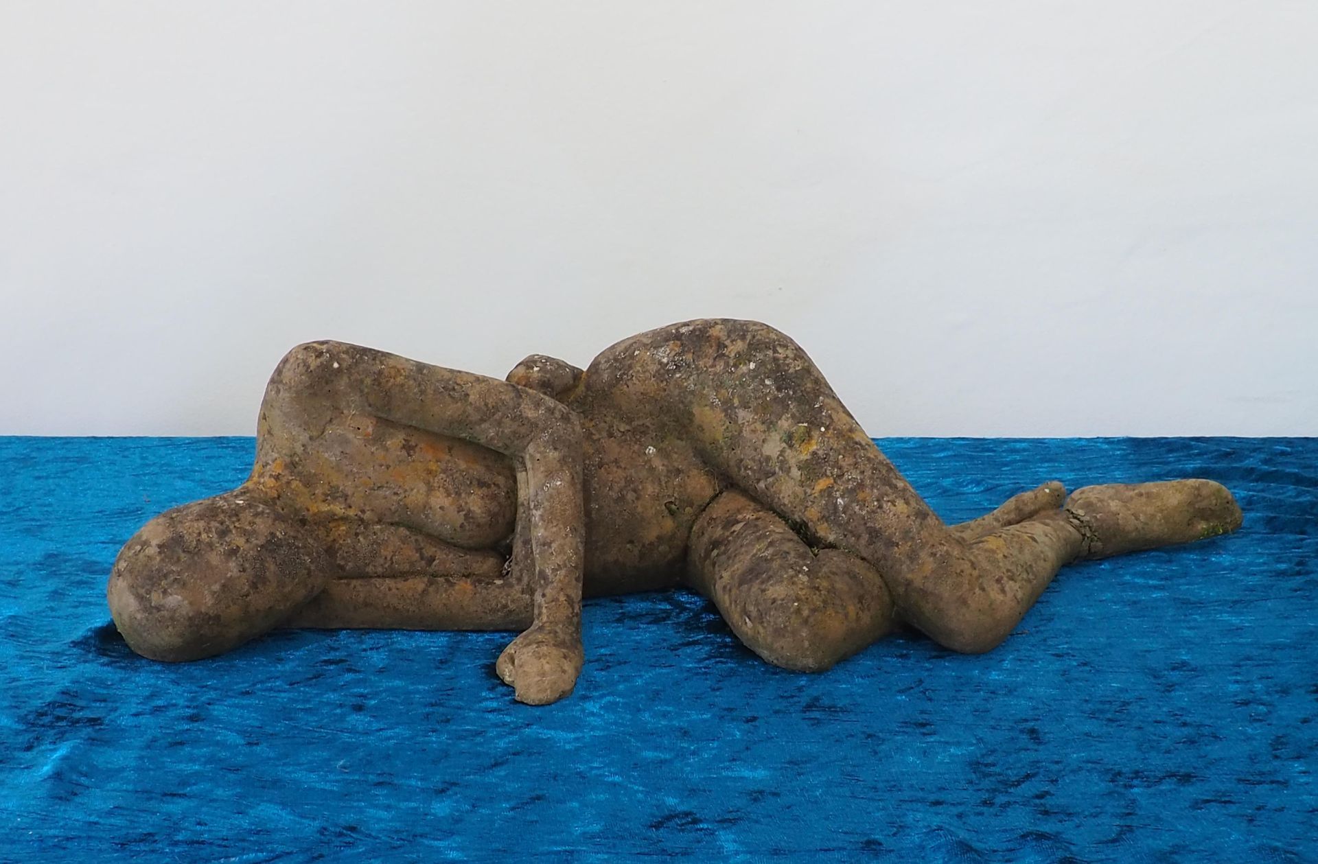 The front of a reclining sculpture of a naked woman. Brown in colour and is on a blue crush velvet surface.