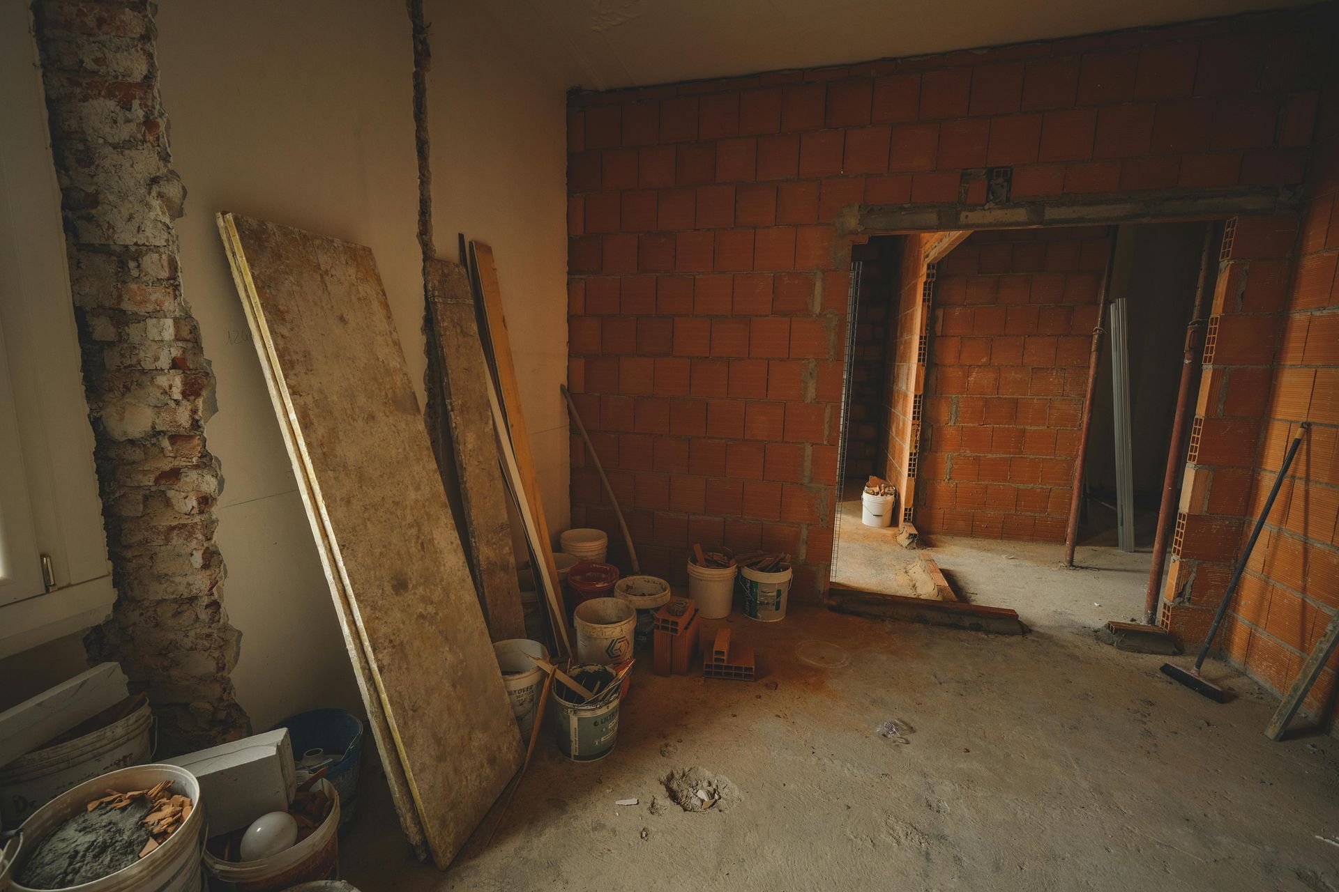 Interior of a building under construction. Exposed brick, concrete floor, wooden planks, buckets, and tools.
