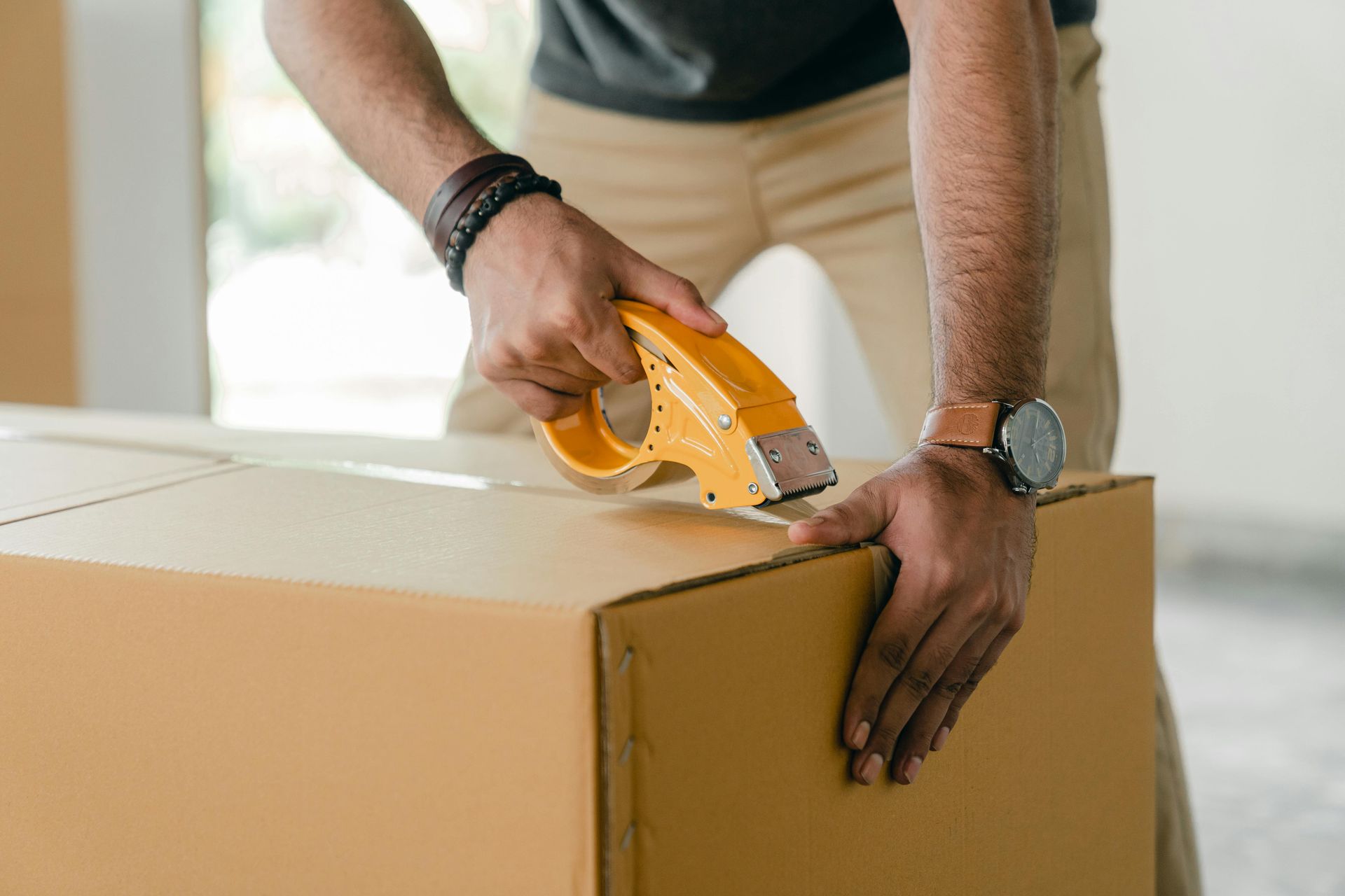 Person sealing a cardboard box with yellow tape.