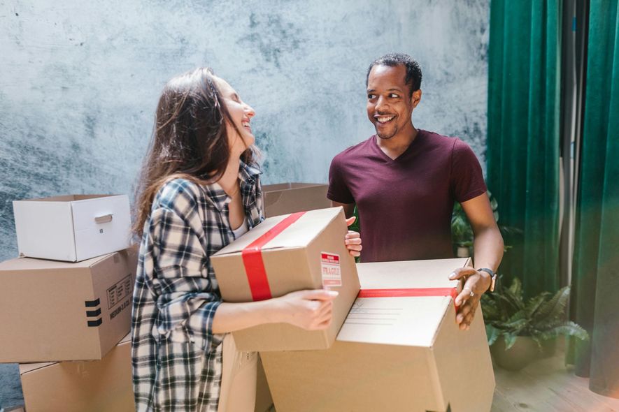 Couple laughing while carrying moving boxes in new home.