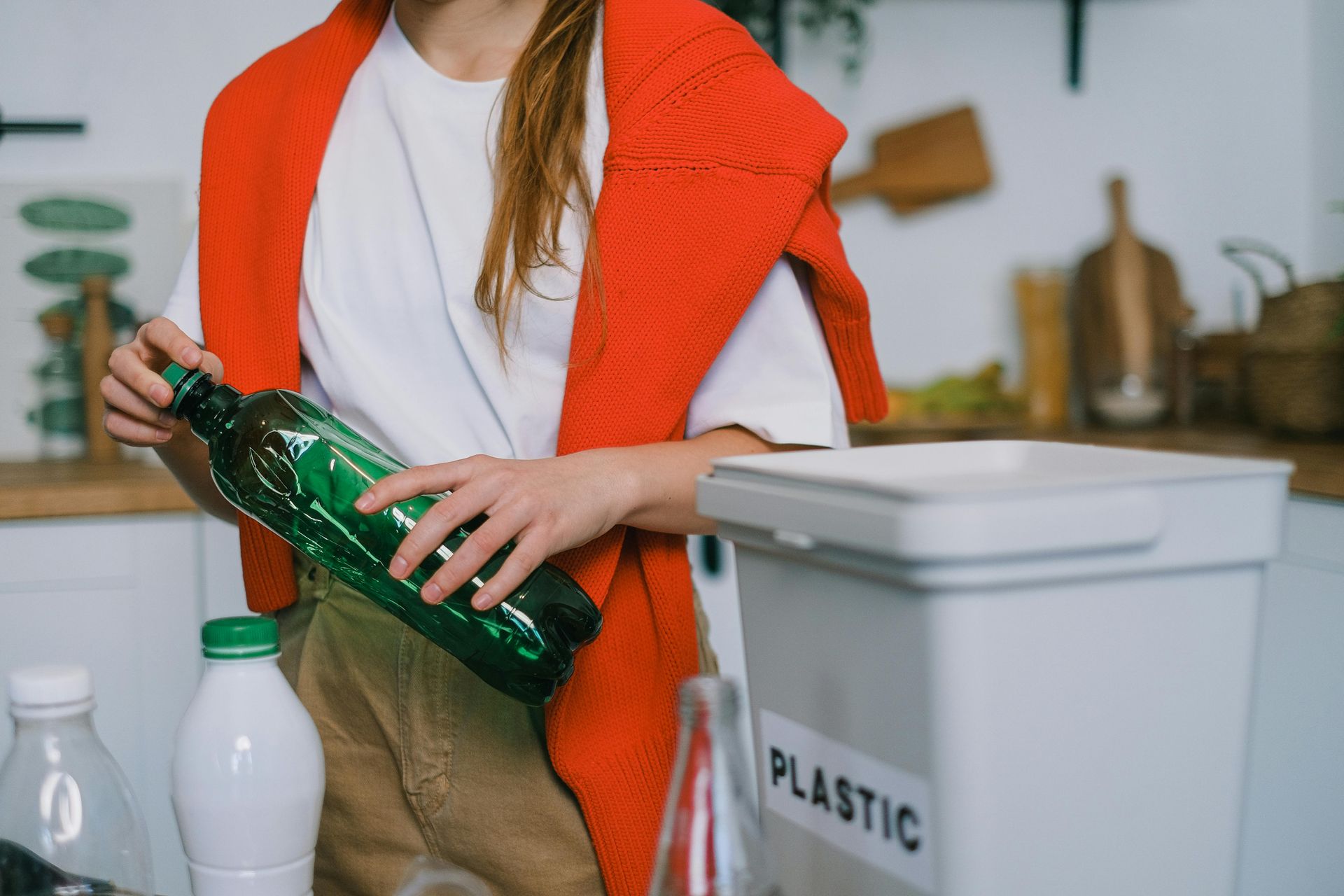 Person putting a green plastic bottle into a plastic recycling bin labeled 