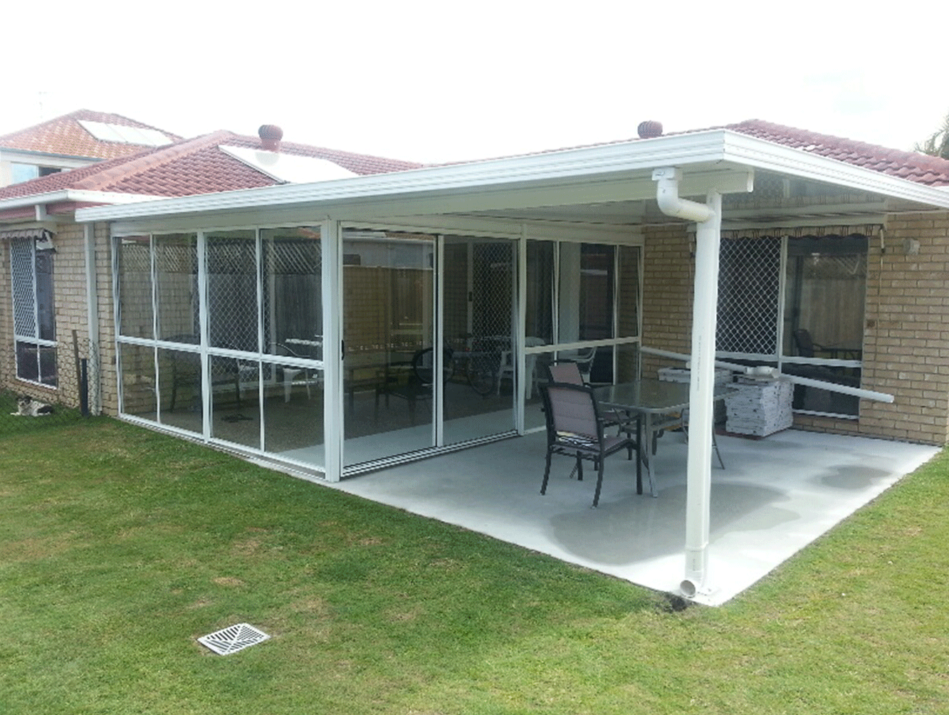 Covered patio with white posts, glass panels, and outdoor chairs beside a lawn