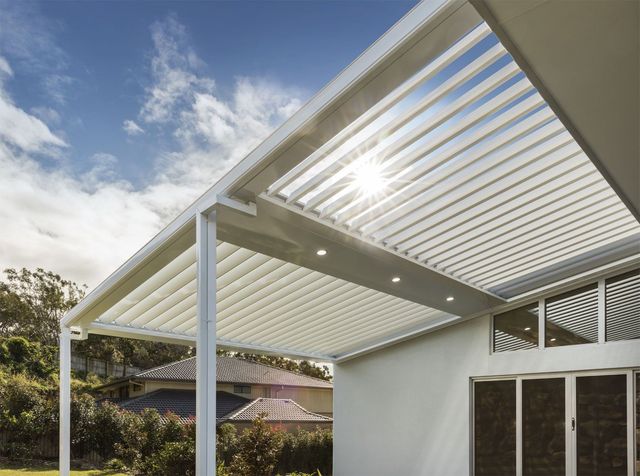 White slatted patio pergola attached to a house, casting shade in a sunny backyard