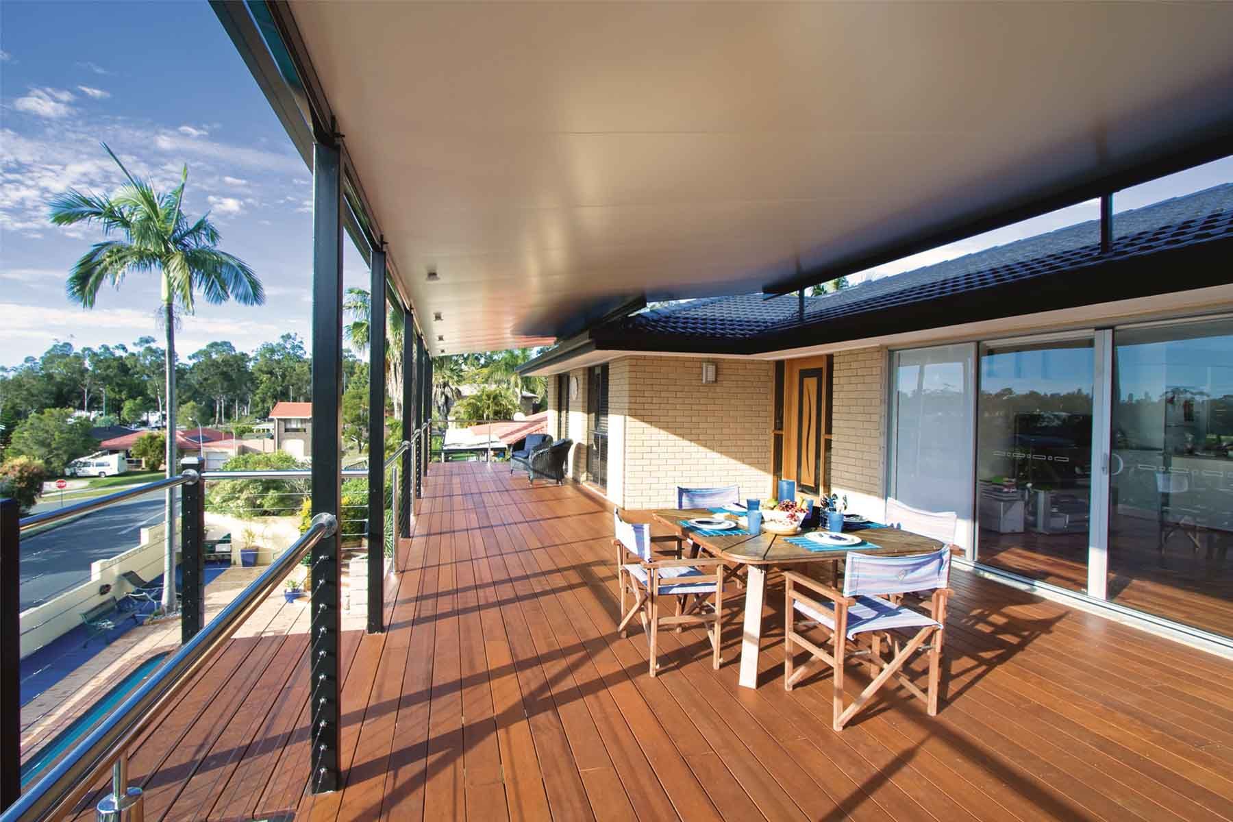 Covered wooden deck with outdoor dining table, chairs, and a view of palm trees and the street