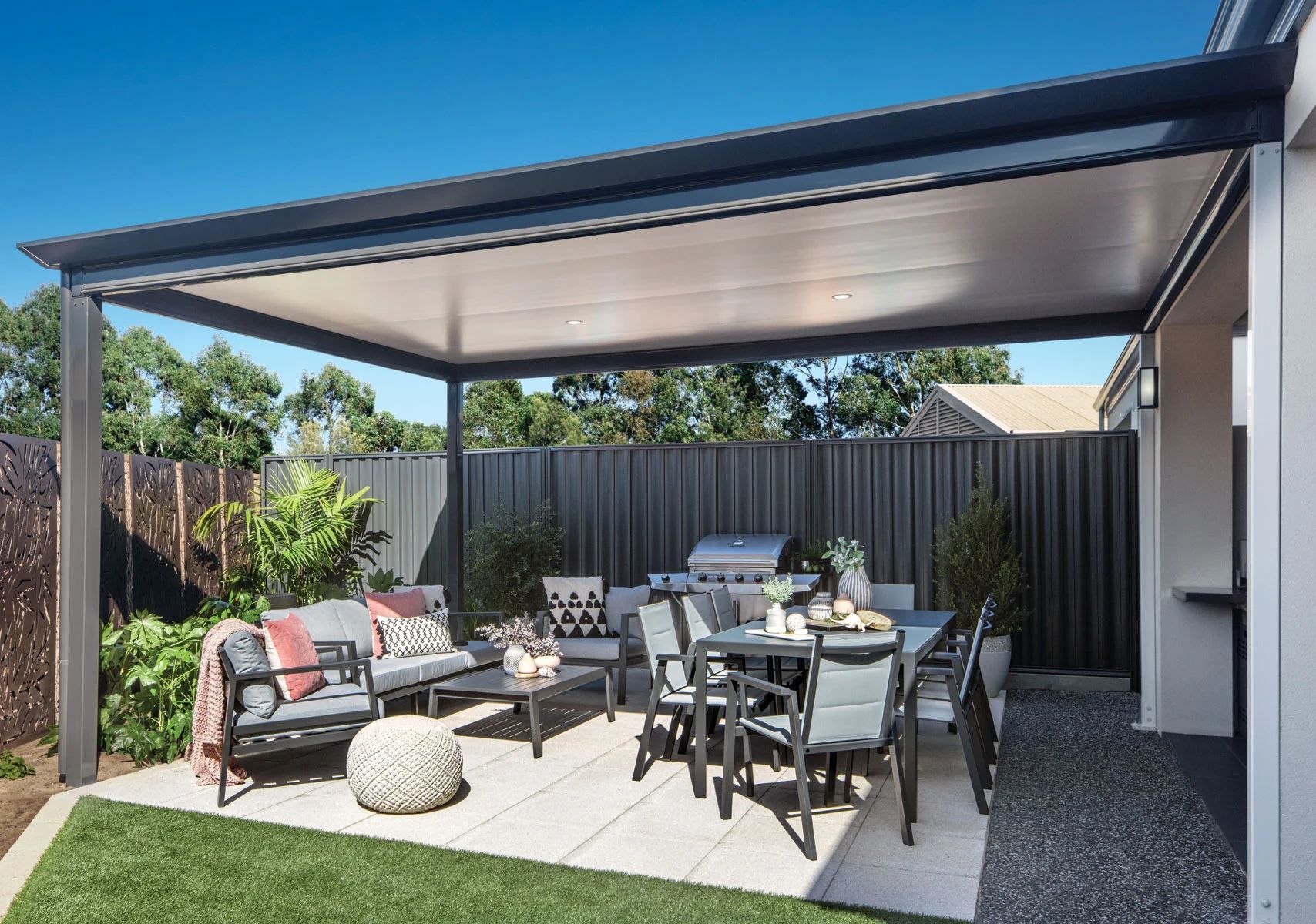 Modern patio with outdoor dining and lounge furniture under a covered pergola in a backyard.