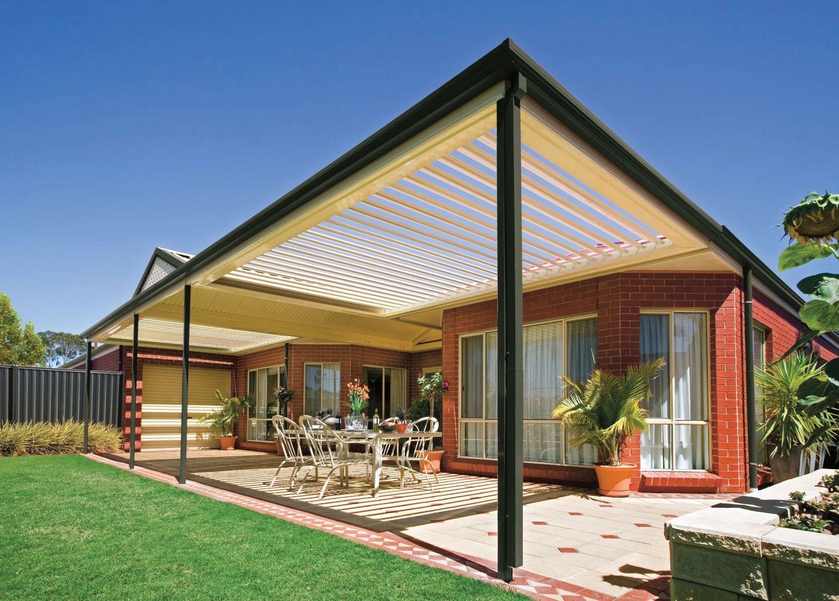 Modern house with a covered patio, outdoor dining set, and green lawn under a clear blue sky