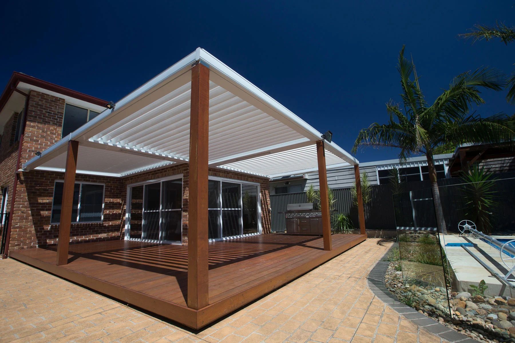 Modern wooden pergola deck beside a brick house under a striped white canopy on a sunny day