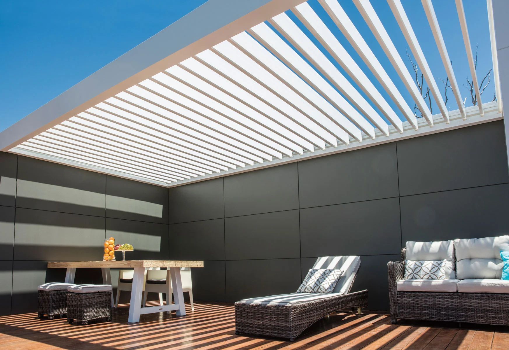 Modern rooftop patio with lounge chairs, a table, and striped pergola shade under a blue sky