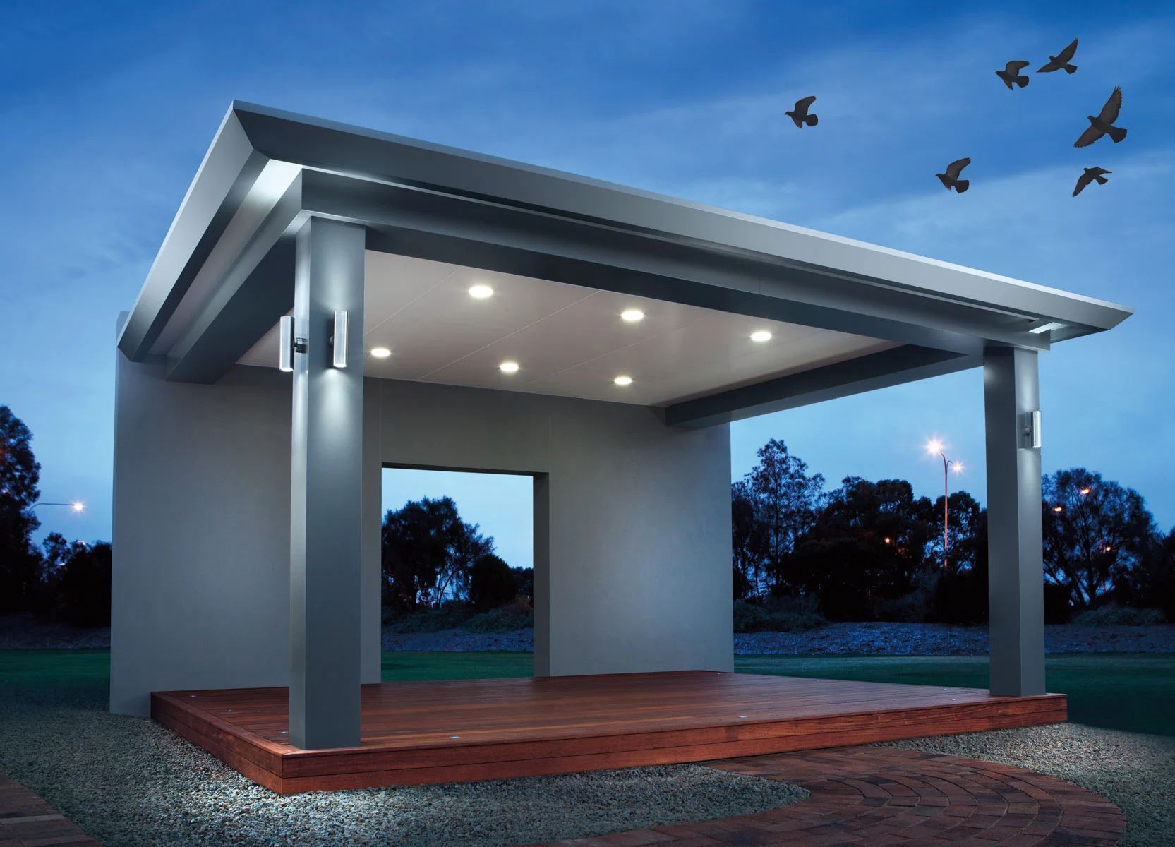 Modern open-air pavilion with a flat roof, lit ceiling lights, and birds flying at dusk