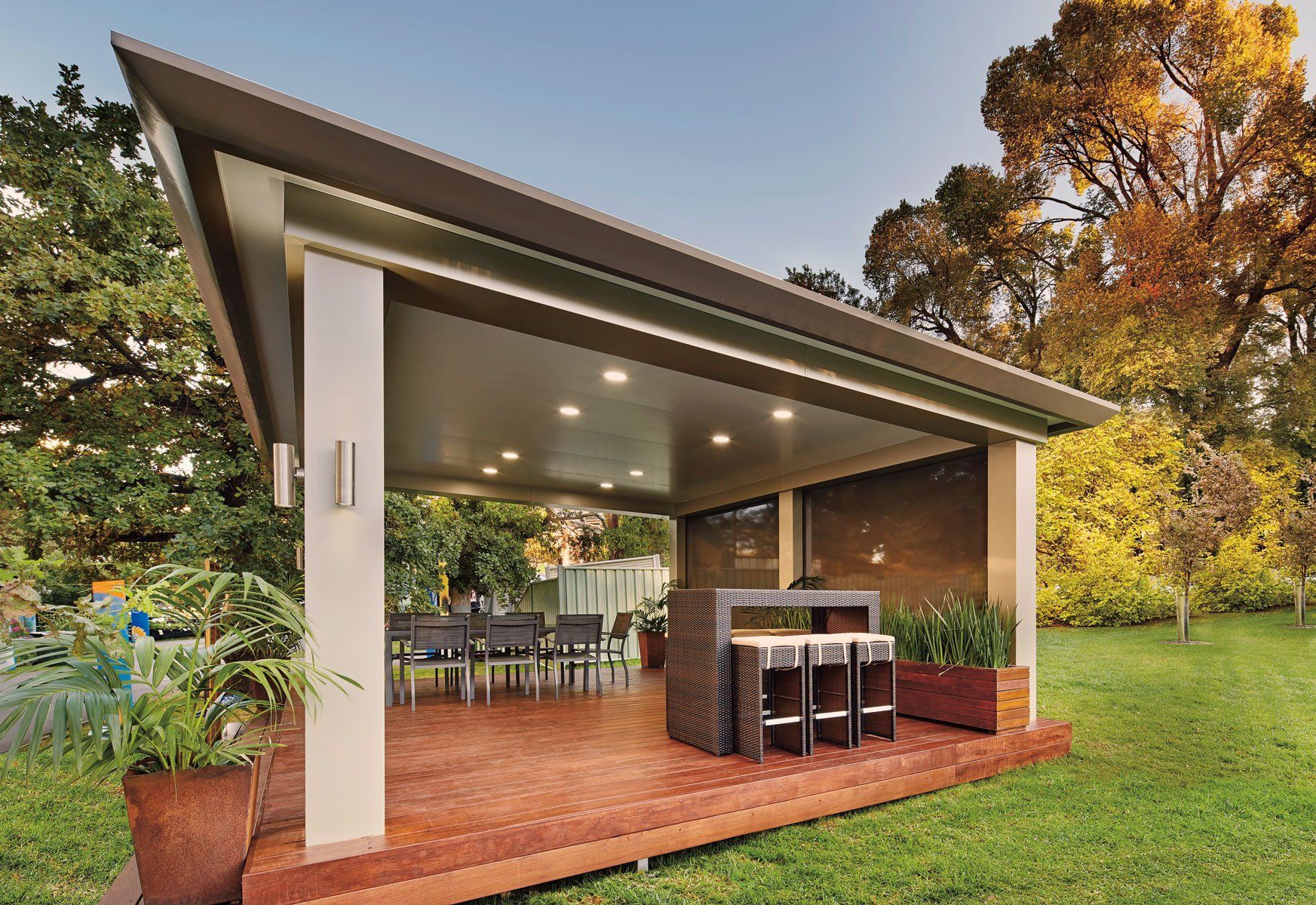 Modern outdoor patio pavilion with dining table, bar stools, and brick flooring in a grassy backyard
