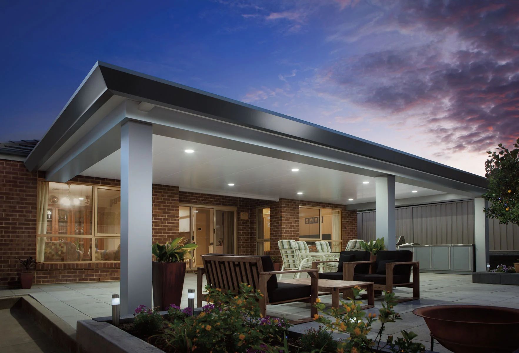 Modern covered patio with outdoor seating beside a brick home at dusk