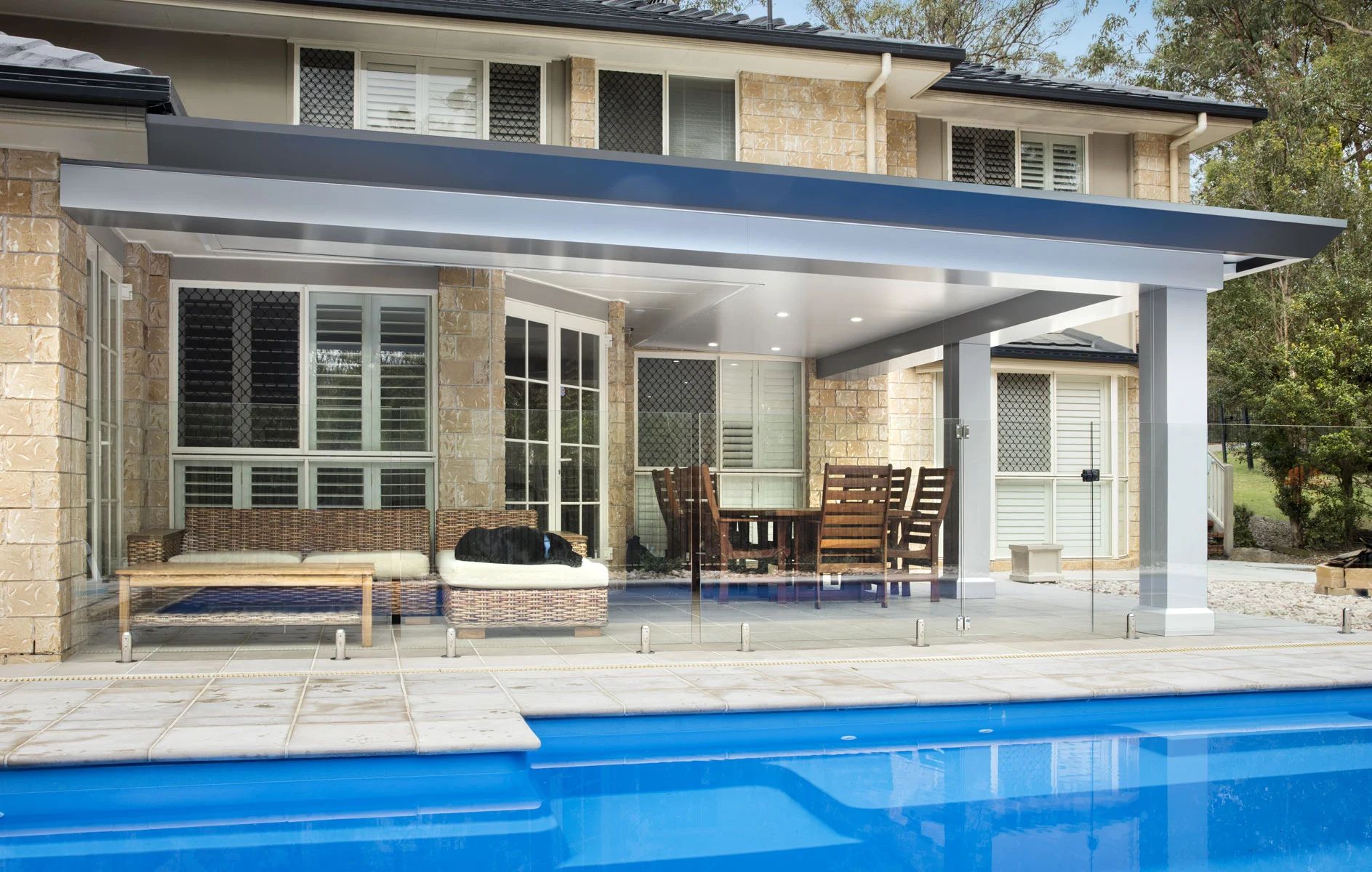 Modern house patio with covered seating area beside a blue swimming pool