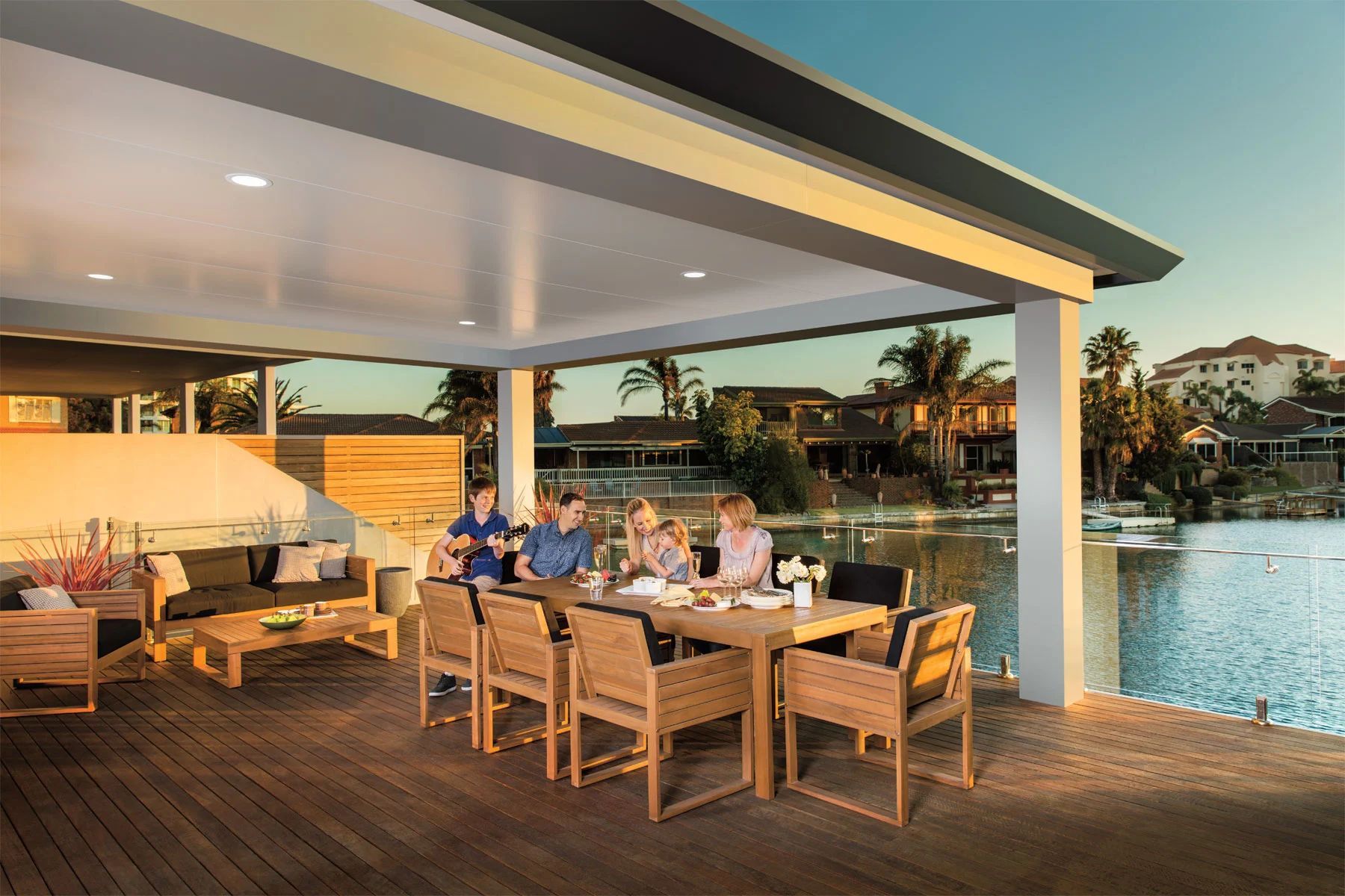 People dining on a waterfront patio at sunset, with warm lights and boats on the water