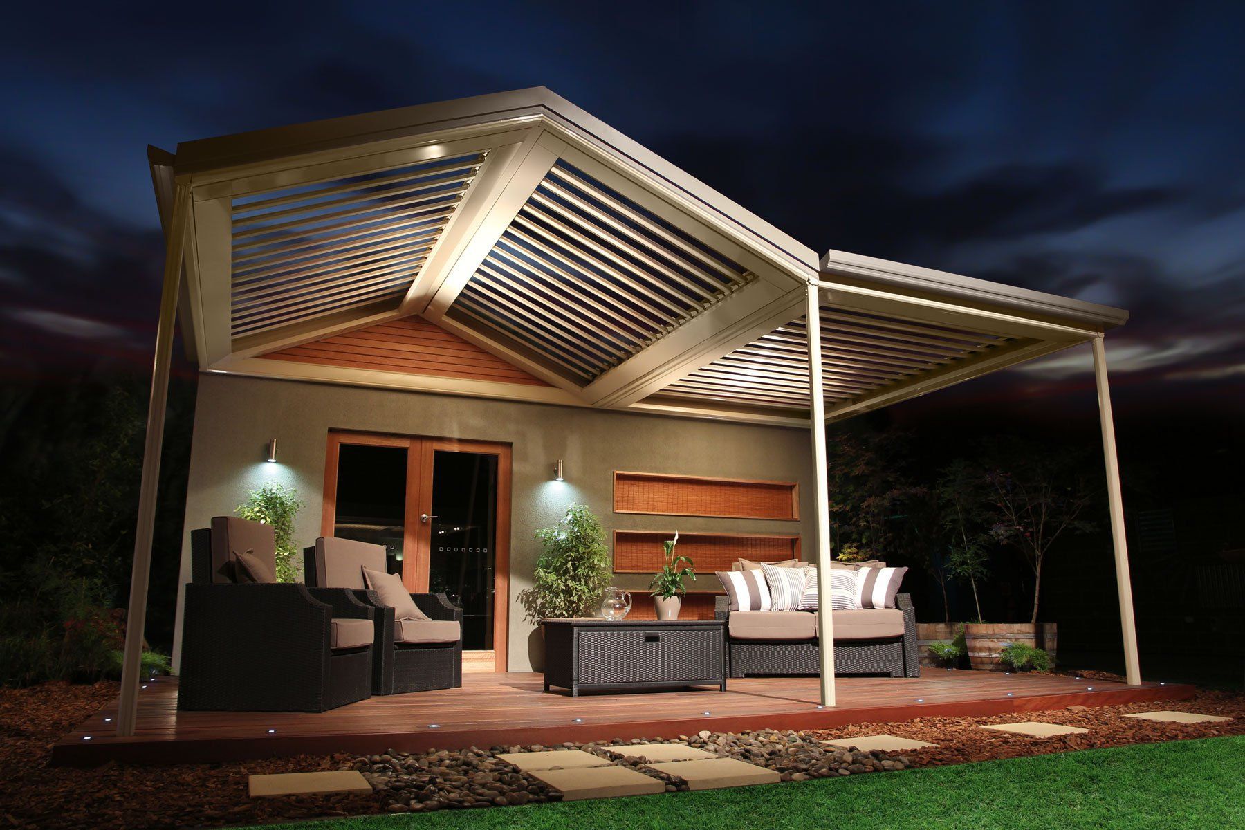 Modern outdoor patio with a lit pergola, wicker seating, and a house entrance at dusk