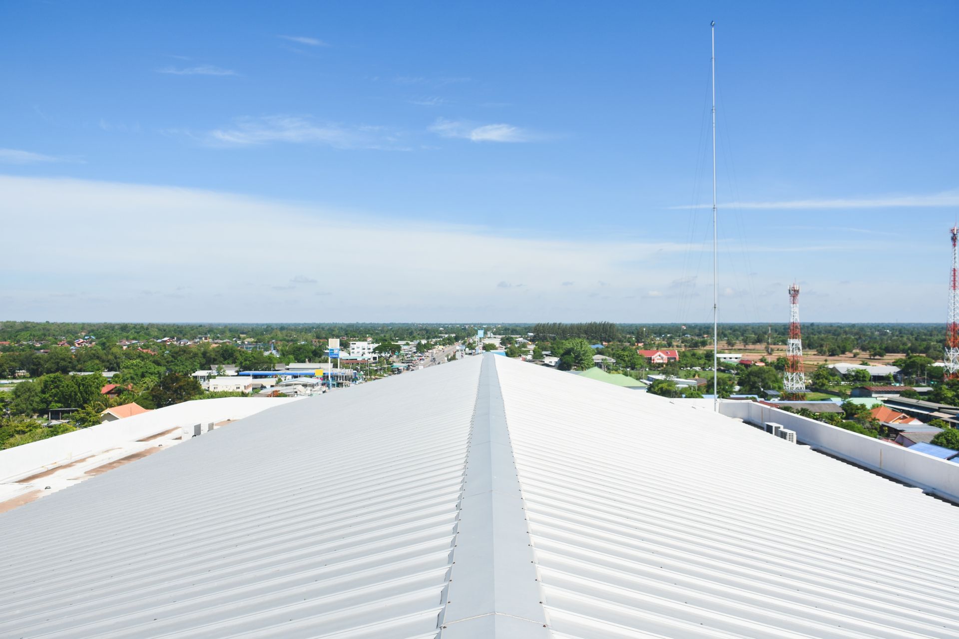 View from a building roof with a long, corrugated metal surface. Distant town under blue sky.