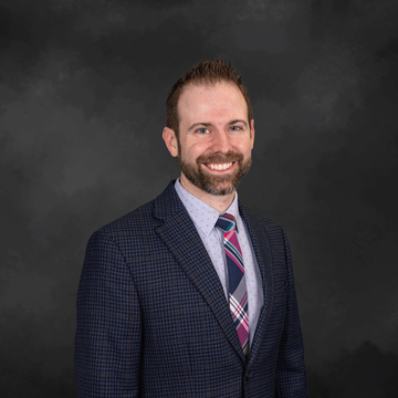 Smiling man in a navy suit and striped tie against a dark studio backdrop