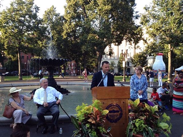 A man stands at a podium in front of a fountain