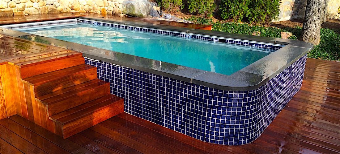 A large swimming pool with stairs leading to it on a wooden deck.