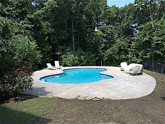 A large swimming pool surrounded by trees and chairs in a backyard.