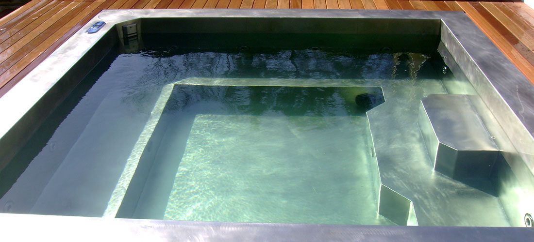 A stainless steel hot tub is sitting on top of a wooden deck.