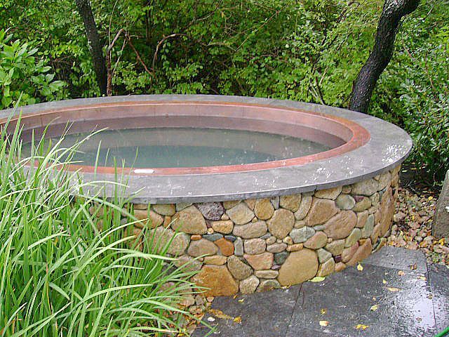 A round hot tub is surrounded by rocks and grass.
