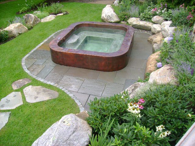 A hot tub is surrounded by rocks and flowers in a garden